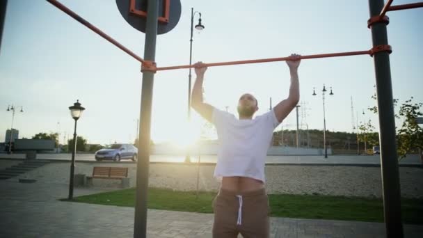 Homem jovem musculoso fazendo pull-ups na barra horizontal. Na área de treino perto de casa - Filmagem, Vídeo