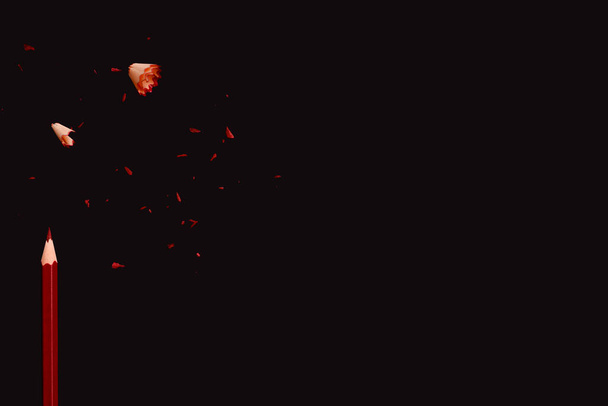 Lápiz rojo con residuos de afilado sobre fondo oscuro, borde lateral de la vista superior. Espacio vacío para texto. - Foto, Imagen