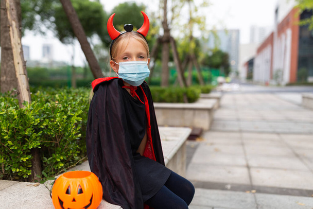 Portrait of cute Little Girl in costume of evil at home. Happy Halloween during coronavirus covid-19 pandemic quarantine concept. Kid wearing medical mask. High quality photo - Photo, image