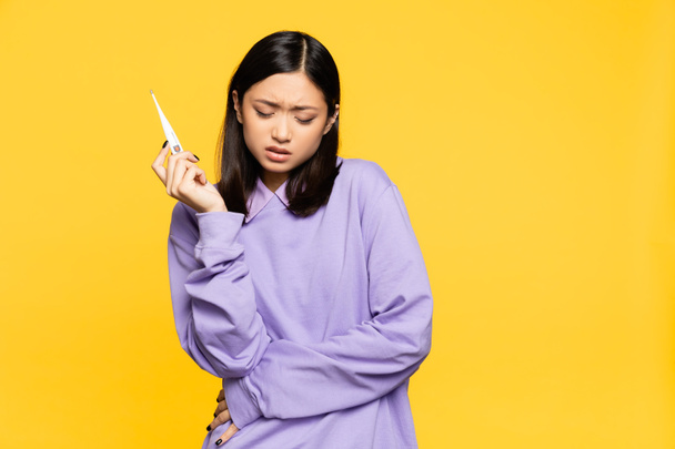sick asian woman holding digital thermometer isolated on yellow  - Photo, Image