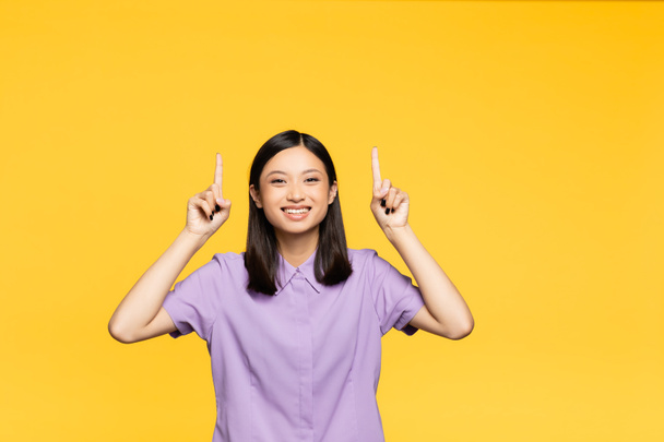 gelukkig aziatische vrouw wijzend met vingers geïsoleerd op geel  - Foto, afbeelding