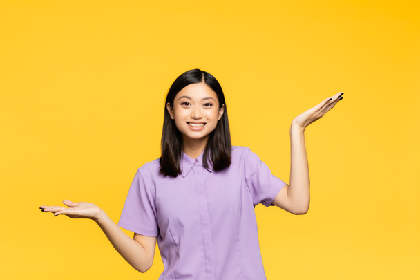 šťastný asijské žena ukazující s rukama izolované na žluté - Fotografie, Obrázek