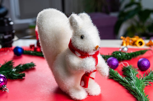 Christmas toy white squirrel on a red background in a red scarf with Christmas entourage - Fotografie, Obrázek