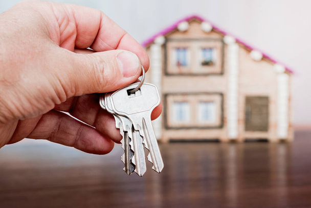 Мужчина держит ключи в руке на заднем плане дома. Продажа и покупка жилья - Фото, изображение