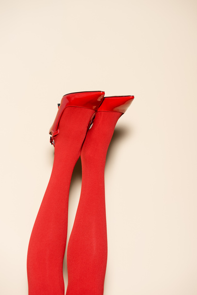 ostříhaný pohled na ženské nohy v červených punčocháčích a obuvi na béžovém pozadí - Fotografie, Obrázek