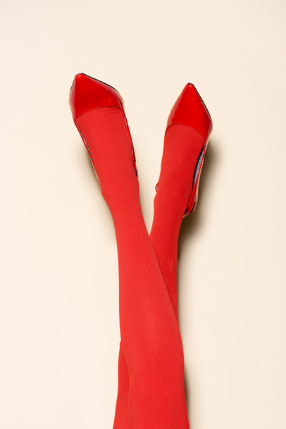 vue recadrée des jambes féminines en collants et chaussures rouges sur fond beige - Photo, image