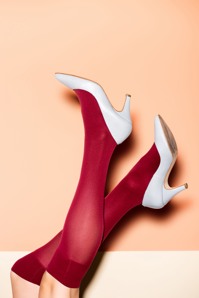 cropped view of female legs in red socks and blue shoes on peach background - Foto, afbeelding