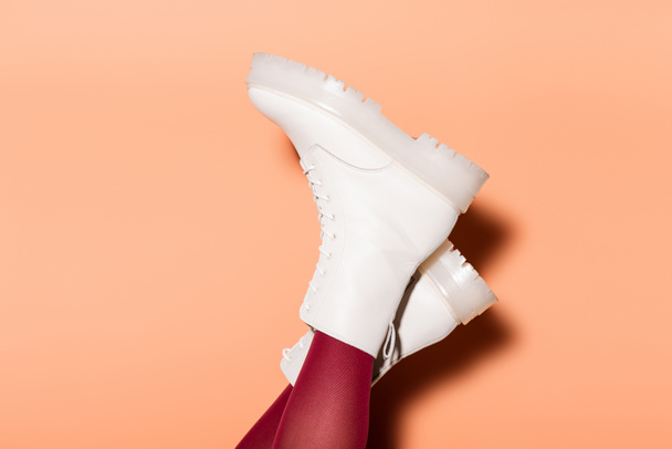 cropped view of female legs in red tights and white boots on peach background - Photo, Image