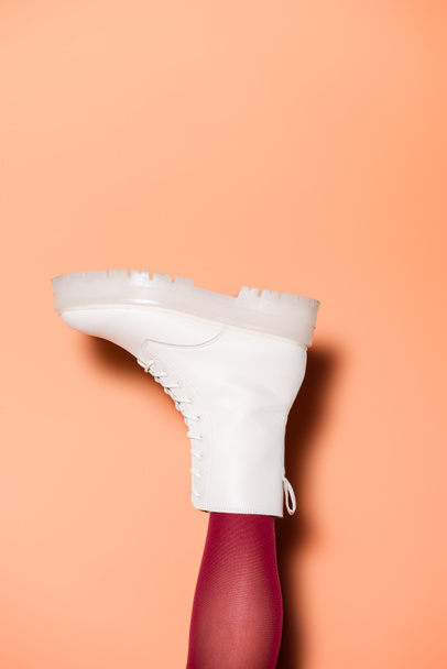 cropped view of female leg in red tights and boots on peach background - Foto, afbeelding