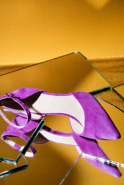 elegante violette suède hakken schoen op spiegel oppervlak op gele achtergrond - Foto, afbeelding