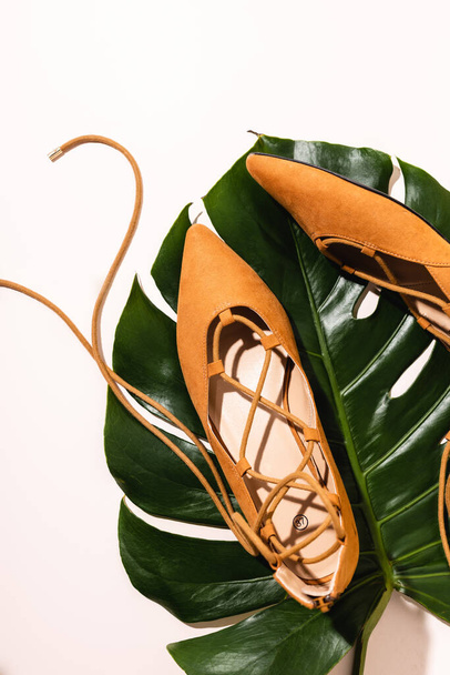 bovenaanzicht van platte suède bruine schoenen op palmblad op beige achtergrond - Foto, afbeelding