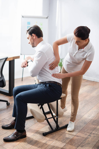 Masseuse doing seated massage of businessman back in office on blurred background - Photo, Image