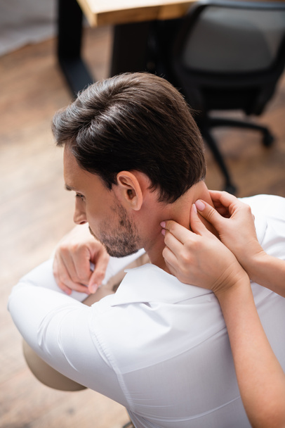 Vista aerea del massaggiatore femminile che massaggia il collo del cliente in ufficio su sfondo sfocato - Foto, immagini