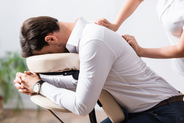 Side view of masseuse doing back massage for client on blurred background - Φωτογραφία, εικόνα