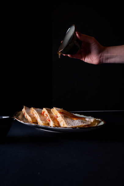 A vertical shot of female hand pouring a sauce into appetizing chicken quesadilla on black background - Foto, afbeelding