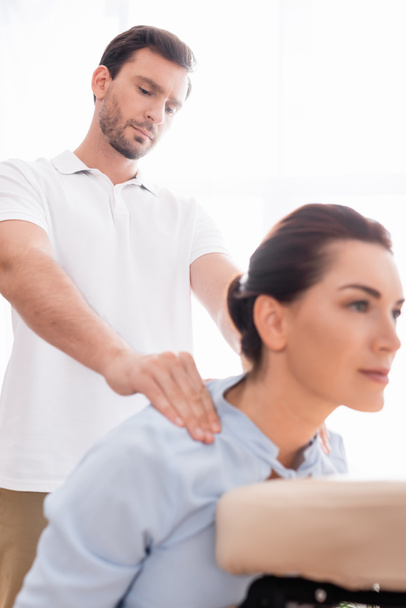 Masseur concentré faisant massage des épaules du client féminin positif sur le premier plan flou - Photo, image