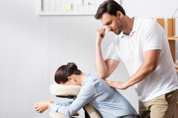 Smiling masseur massaging businesswoman back with elbow in office on blurred background - Photo, Image
