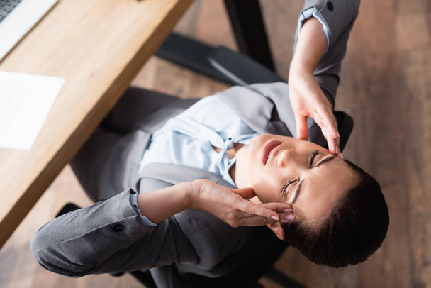 Widok wyczerpanej bizneswoman z migreną siedzącej na fotelu biurowym na rozmytym tle - Zdjęcie, obraz