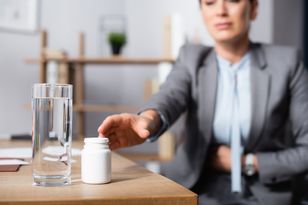 Cropped view of businesswoman with stomachache taking medication on blurred background - Foto, afbeelding