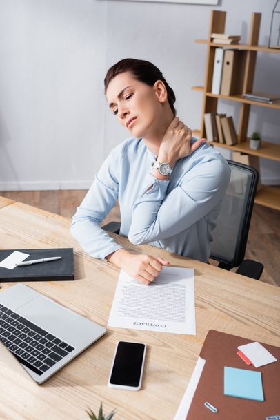 Femme d'affaires avec un cou blessé assis sur une chaise de bureau sur le lieu de travail - Photo, image