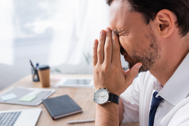 Side view of tired businessman with praying hands, suffering from headache with blurred workplace on background - Photo, image