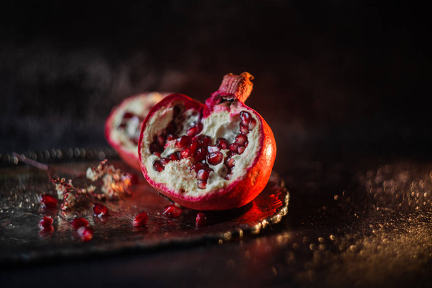 halves of pomegranate with sprinkled grains on a beautiful vintage tray on a dark background - Foto, Imagen