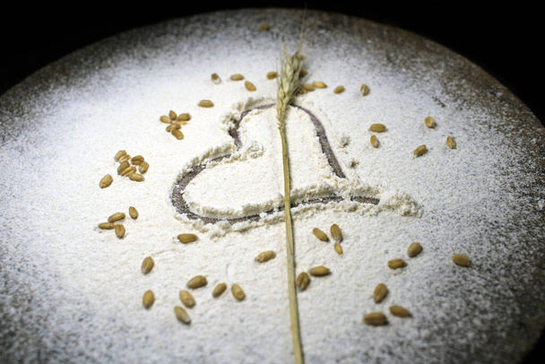 Grain de blé frais récolté sur fond de farine de blé. Concept de cuisson sur fond de bois, saupoudrer de farine avec le cœur. Coeur dessiné en farine éparpillée à côté d'un rouleau à pâtisserie en bois sur fond bois - Photo, image