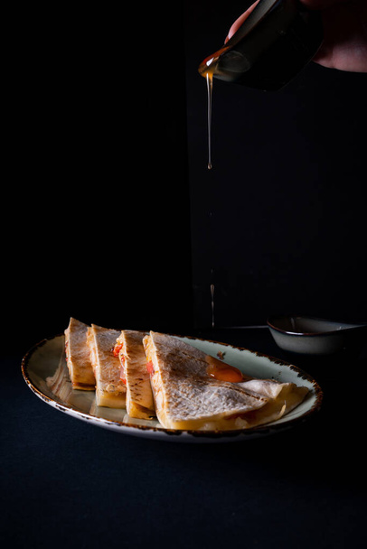 A vertical shot of a person pouring ketchup plate with quesadilla on a black background - Fotoğraf, Görsel