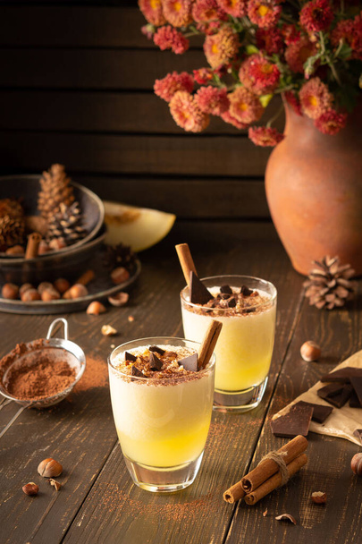 Frissítő ízletes dinnye smoothie fahéjjal, mogyoróval és csokoládéval, váza krizantém és üveg smoothie fából készült háttér - Fotó, kép