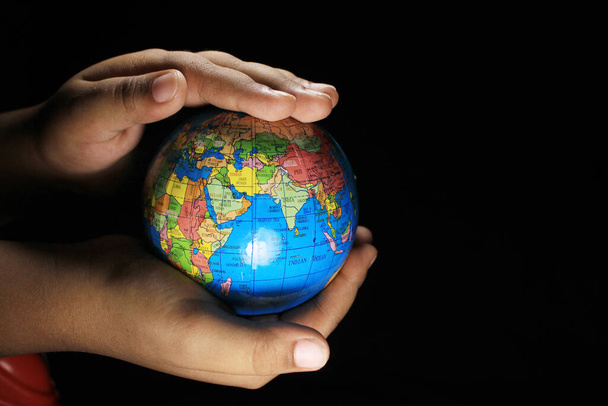 Child hands holding the Earth globe on black background. Earth globe isolated on a black background. School globe on black background. - Фото, зображення
