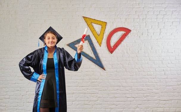 Chica graduada y ropa de graduación en frente de la pared de ladrillo blanco, certificado y estilo de fondo regla. - Foto, Imagen