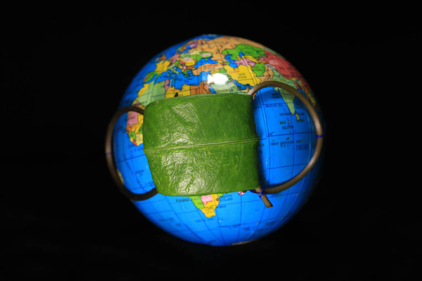 Омоложення Землі під час ситуації Кові19. Концепція коронавірусу у світі та пандемії COVID-19. Глобус захищений зеленим листям. Концептуальна фотографія. Земля ізольована на чорному тлі - Фото, зображення