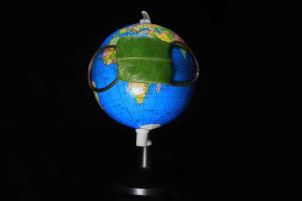 Rejuvenation of earth during Covid19 situation. Concept of Coronavirus in world and COVID-19 pandemic. Globe protected by green leaf. Conceptual photography. Earth globe isolated on a black background - Photo, Image
