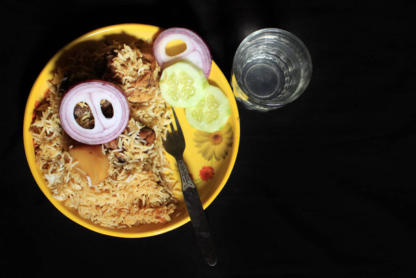 Вкусный вкусный индийский курица Biriyani на желтой пластине изолированы на черном фоне. Индийская курица Biriyani Карри Фуд с огурцом и луком. Индийский цыпленок Тикка Биряни Карри.  - Фото, изображение