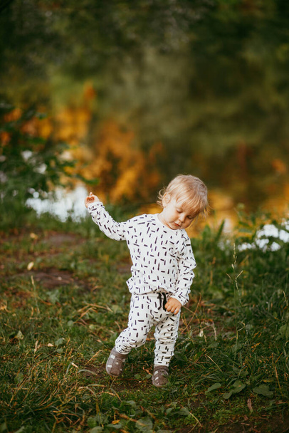 Cute boy walking in a beautiful white suit against the background of nature, baby about one year old learning and playing outdoors. - Foto, imagen