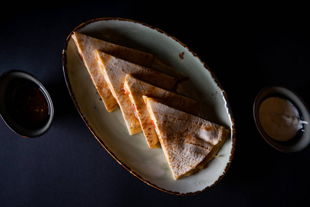 A top view of a plate with quesadilla on a black background - Foto, Imagem