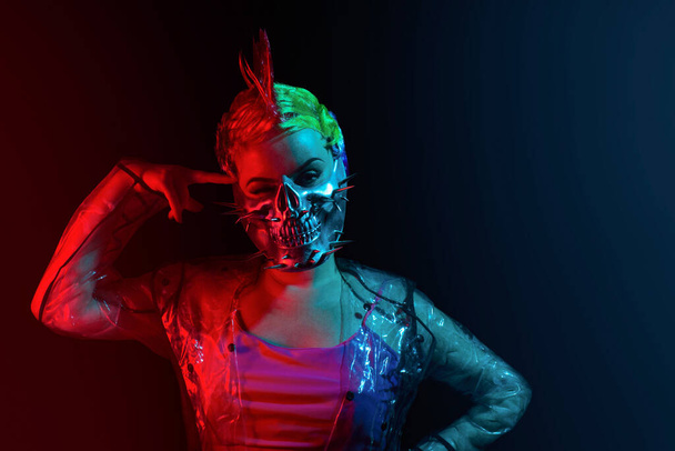 Femme cyberpunk suicidaire folle avec coiffure mohawk dans un masque à pointes avec un doigt sur son front. - Photo, image