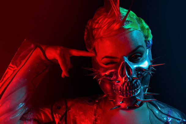 Portrait of suicidal cyberpunk woman with mohawk hairstyle in spiked mask with finger on her forehead. - Photo, Image