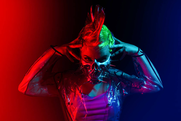 Mujer cyberpunk con peinado mohawk poniéndose una máscara con pinchos. - Foto, imagen