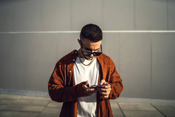 A closeup of a young stylish European man typing a text message on his smartphone - Foto, Bild