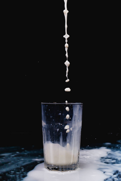 A closeup shot of milk being poured in a glass cup on a black background - Φωτογραφία, εικόνα