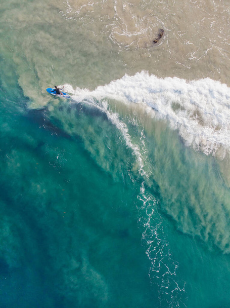 A top view shot of a person with a surfboard swimming in Varkala Beach - Фото, зображення
