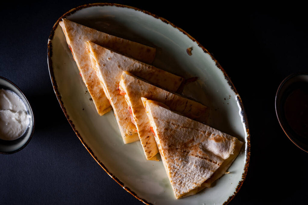 An appetizing chicken quesadilla with sauce isolated on black background - Foto, afbeelding