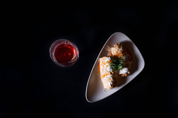 A top view of crepe rolls and a glass of wine on a black background - Foto, afbeelding