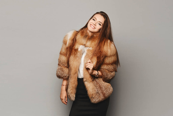 Elegant young woman posing in a luxury fashion fur coat over light grey background, isolated. Winter clothes - Fotografie, Obrázek