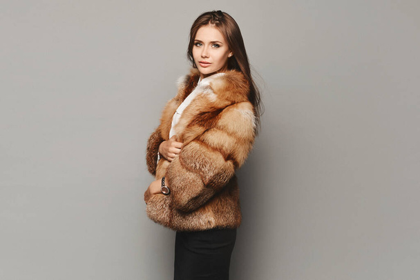Side view of a model girl in a luxurious fur coat at the grey background. Winter fashion - Fotografie, Obrázek