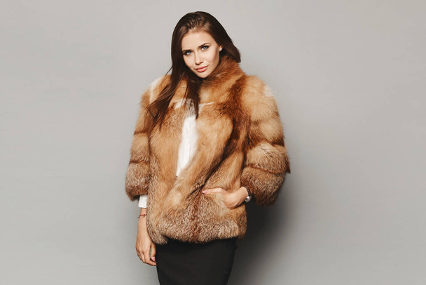 Model girl in a luxurious winter fur coat on the grey background, isolated. Winter fashion - Photo, image