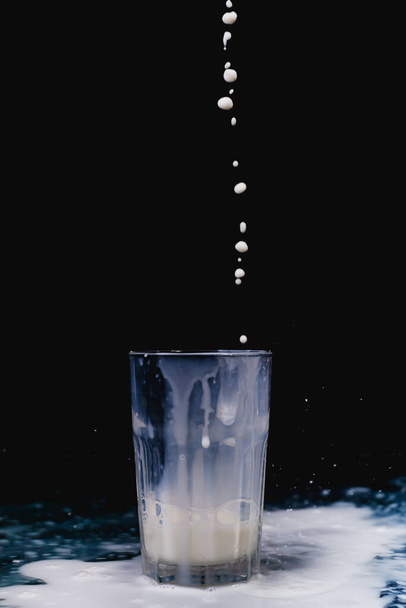 Un primer plano de leche que se vierte en una taza de vidrio sobre un fondo negro - Foto, imagen