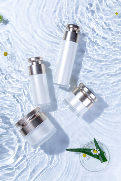 A vertical top view of skincare bottles on a white water surface - Foto, afbeelding