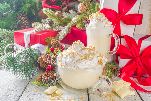 Christmas winter hot chocolates idea, recipe. Cheesecake hot chocolate with cheesecake aroma and crumbs, white chocolate and creamy milk. On white wooden table background with Christmas decor - Photo, Image
